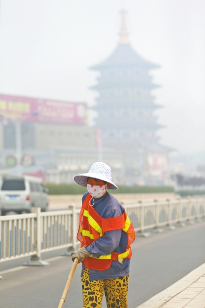近日，在古都洛陽，環(huán)衛(wèi)工人身后的“天堂”被霧霾籠罩著。