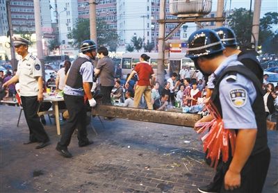 6月13日晚8點，朝陽路和青年路交叉口西側(cè)，一次聯(lián)合執(zhí)法行動中，輔警與協(xié)管抬走商戶的燒烤用具。新京報記者 尹亞飛 攝