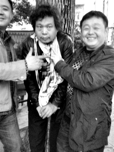 兩名接訪人員與患有癌癥的訪民段新德合影時(shí)，面帶笑容擺出勝利的手勢(shì)。