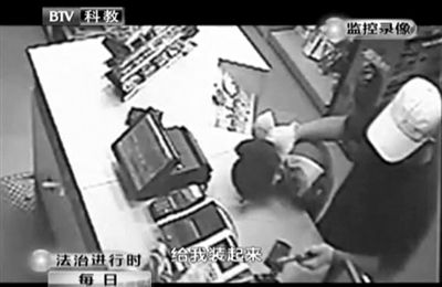 戴帽男子一手掐住加油站營業(yè)員，一手持發(fā)令槍指向另一營業(yè)員，要求“把錢給我裝起來”。