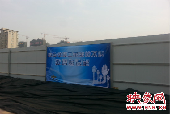 道路南側(cè)圍起了白色的圍擋，墻上標(biāo)示著“因地鐵施工帶來的不便敬請(qǐng)您諒解”的提示牌。