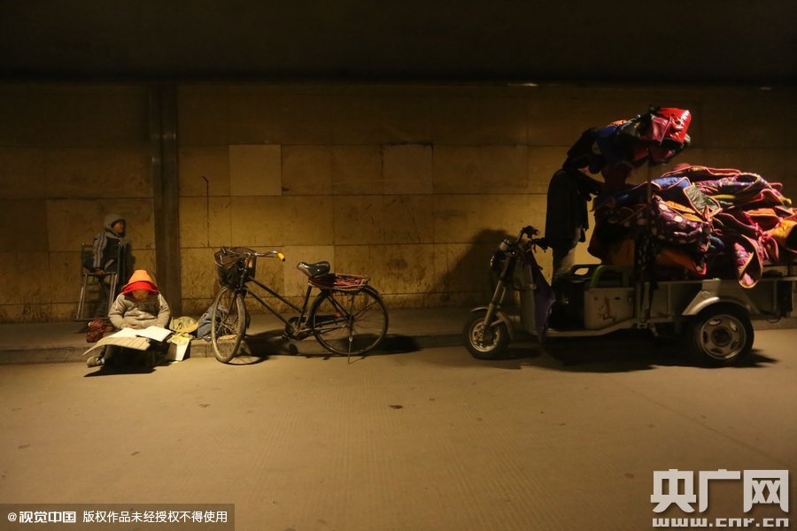 2015年11月8日晚，鄭州，7歲男孩涵洞橋下陪父母練攤，路邊燈下坐小馬扎上寫作業(yè)。