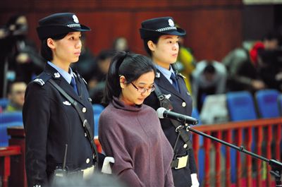 被告人盧梅低著頭，站在朝陽法院刑事審判庭的被告席上。