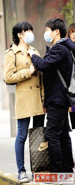 公交站臺上，一對年輕人戴著口罩，系緊衣領。